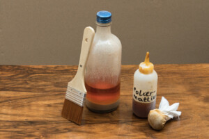 Pinsel, Flasche mit Politur, Flasche mit Aufschrift „Poliermattierung“ und Poliertuch auf Holzoberfläche.