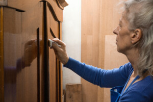 Frau poliert mit Tuch die glänzende Holzoberfläche eines Schranks in einer Werkstatt.